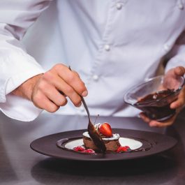 Chef putting chocolate sauce on a dessert in a commercial kitchen